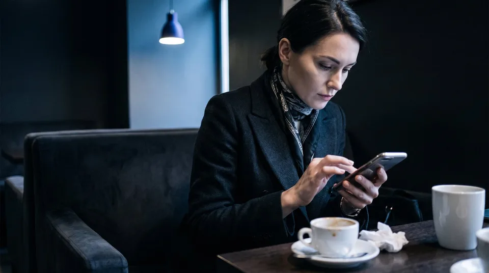 A stylish female marketer swiping through a carousel on her smartphone in a dimly lit cafe.