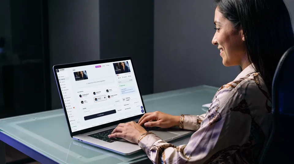 A woman sitting at a desk in a modern, moody office, happily working on her laptop.